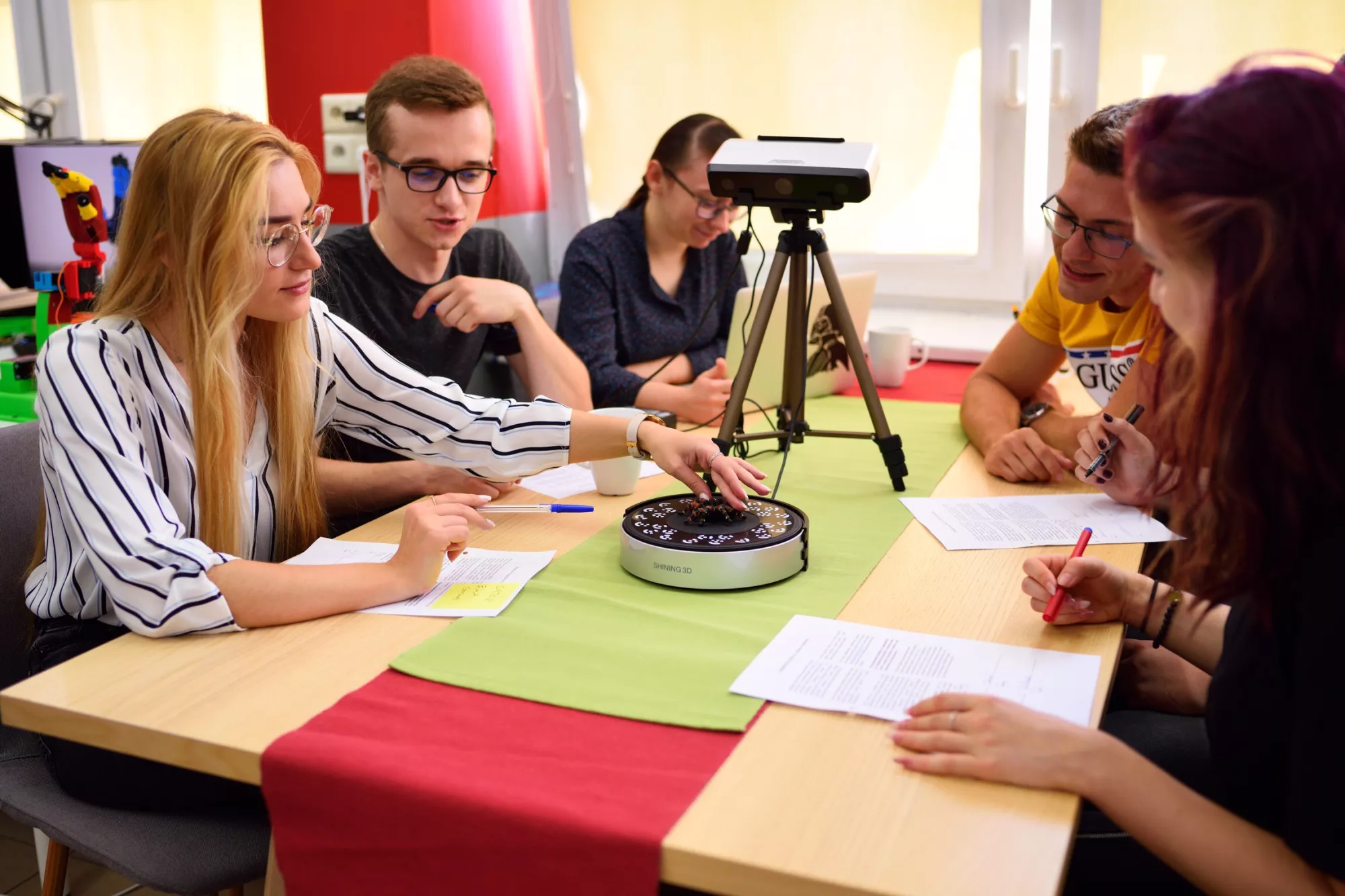 Członkowie SKN UbiComp siedzą przy stole, rozmawiają i robią notatki.