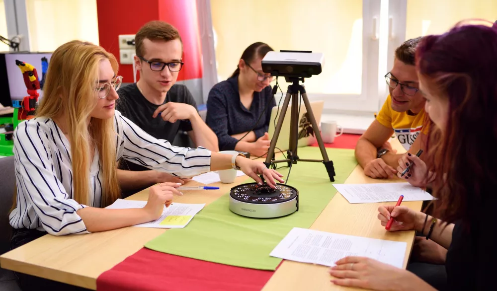 Członkowie SKN UbiComp siedzą przy stole, rozmawiają i robią notatki.