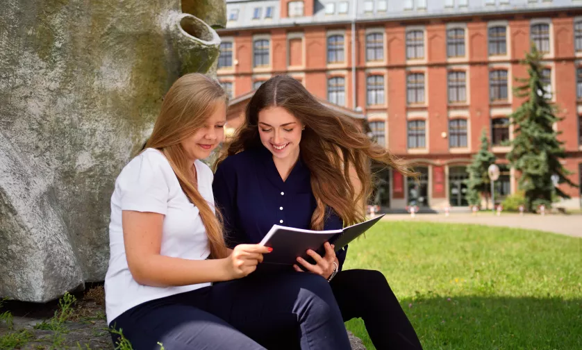 Studentki siedzą przed budynkiem i się uczą.