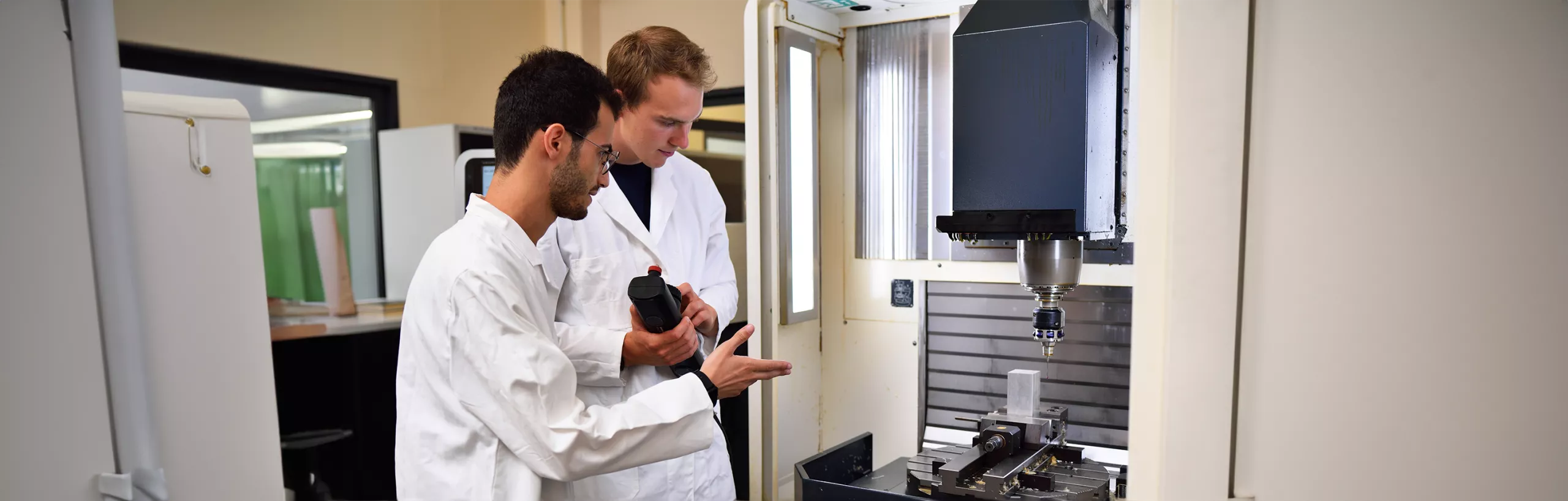 Two students standing next to a scientific device in a mechanical laboratory. 