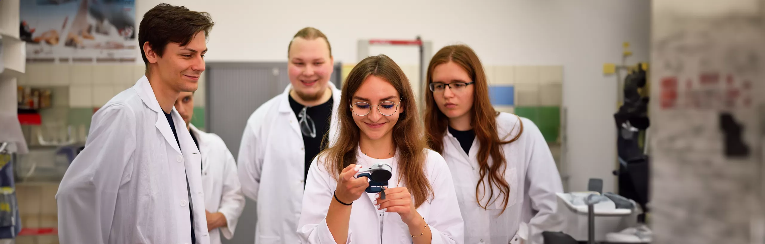 Studenci w fartuchach prowadzą eksperymenty chemiczne.