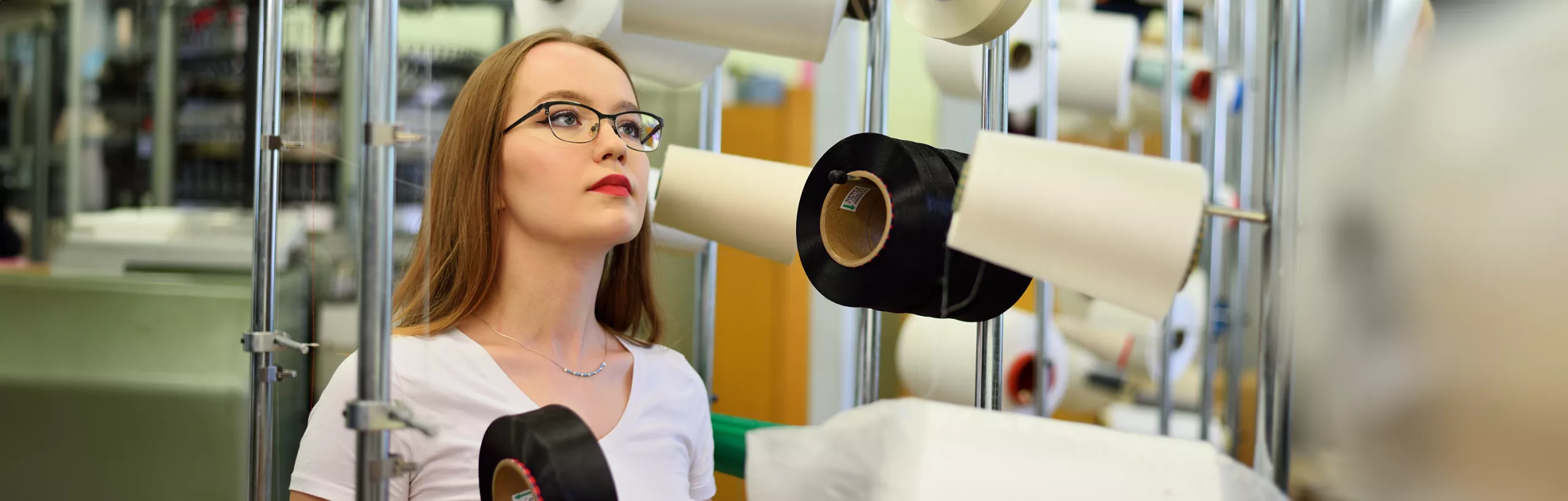 Studentka patrzy na nici w hali produkcyjnej.