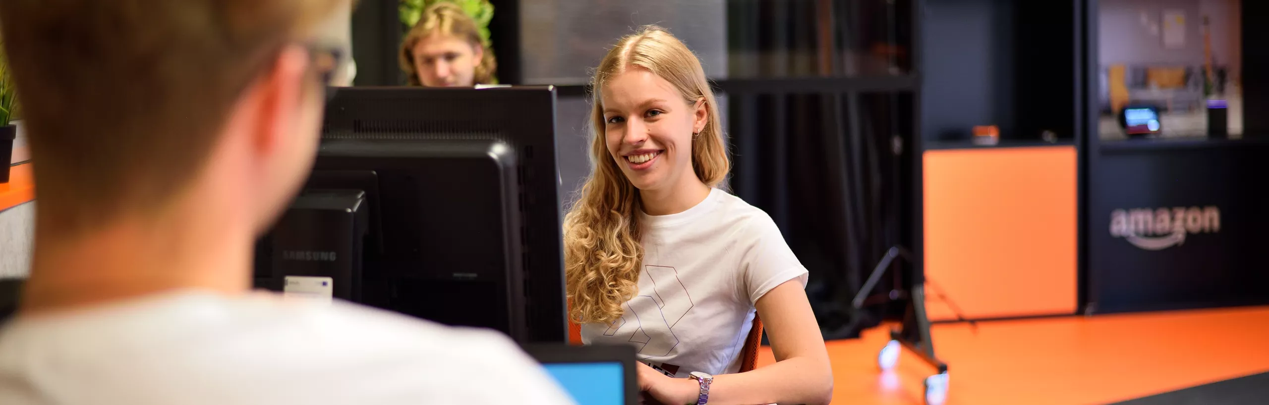 Studentka siedzi przy komputerze i patrzy w obiektyw aparatu.