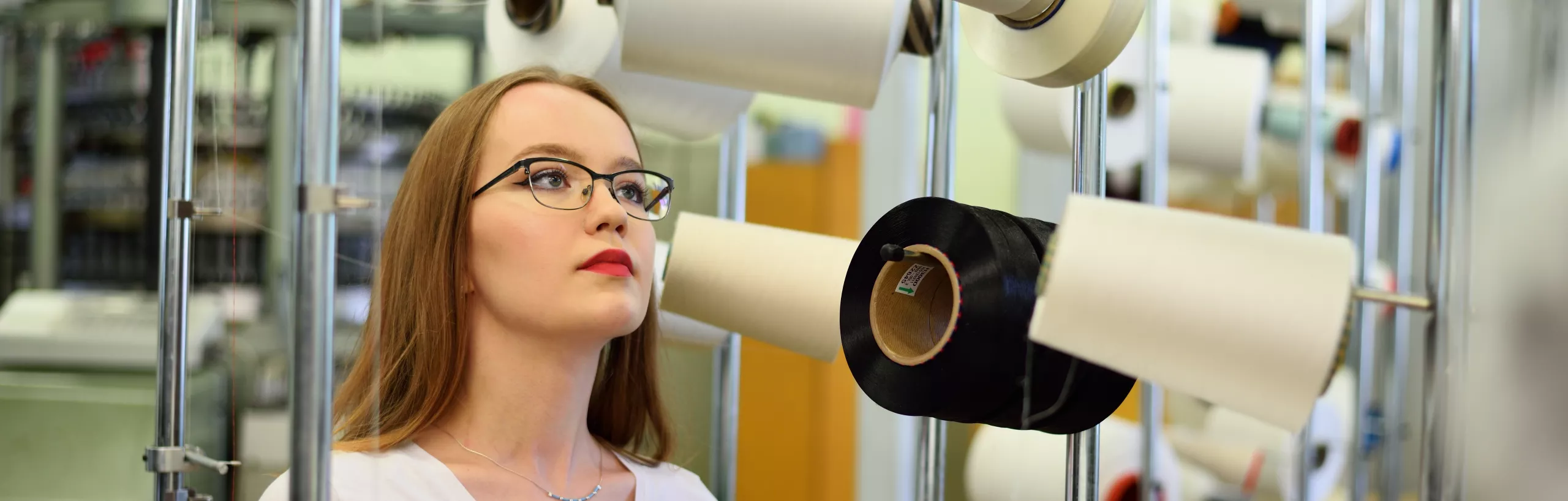 Woman looking at spools of thread in a production hall. 